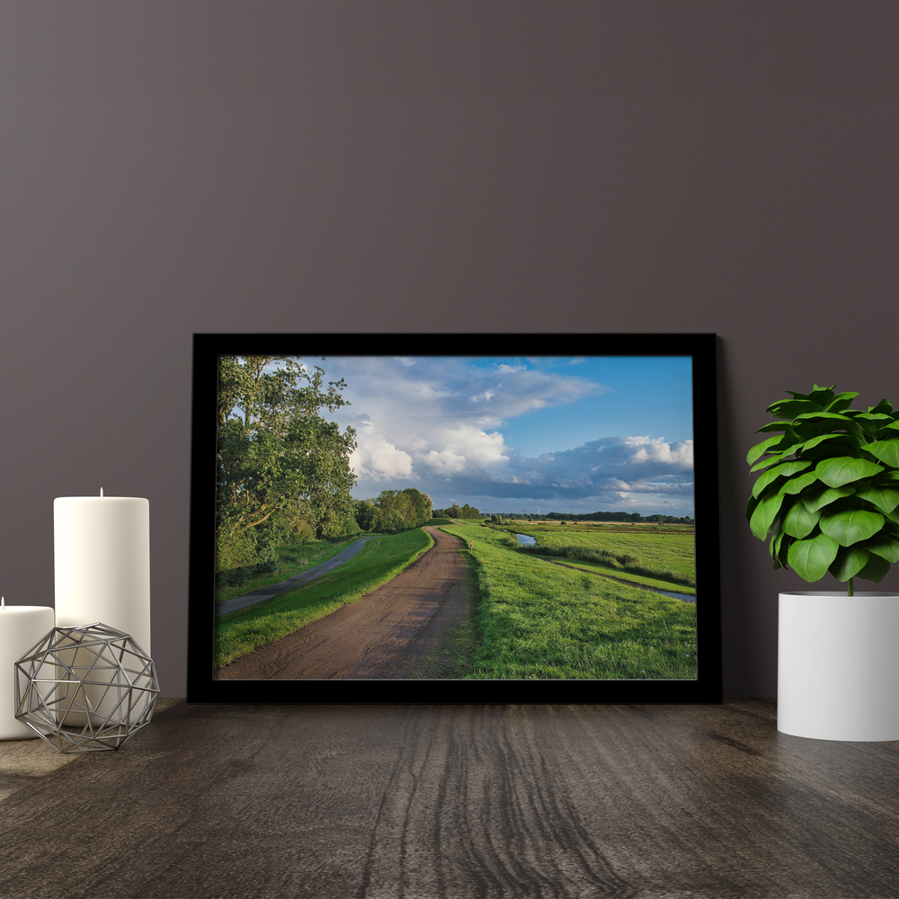 Black-framed acrylic landscape photo print on a wooden surface beside candles and a potted plant
