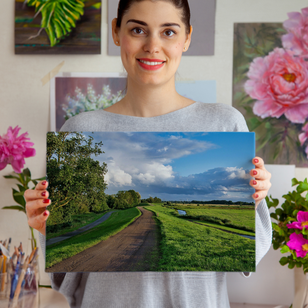 Frameless acrylic photo print of a country path, green meadows and cloudy sky, displayed in front of floral art