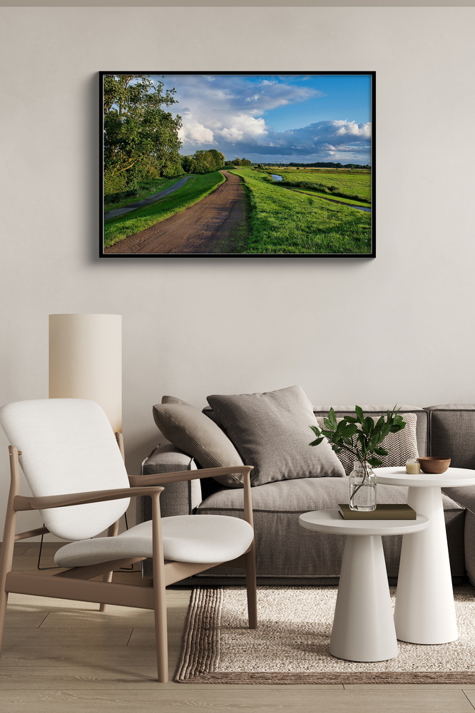 Black-framed acrylic landscape photo print above a sofa beside a light-colored armchair in a neutral living room