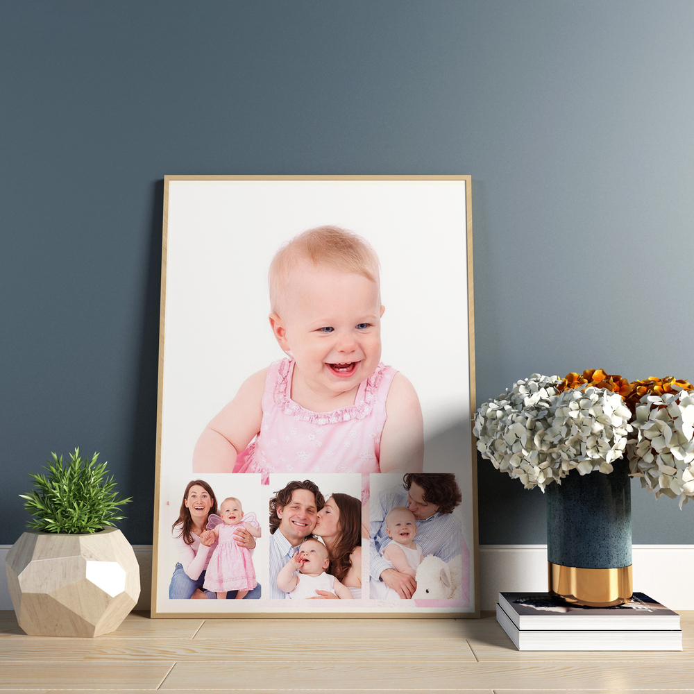 Wood-framed family photo collage with a child portrait on a shelf beside flowers, against a blue-gray wall