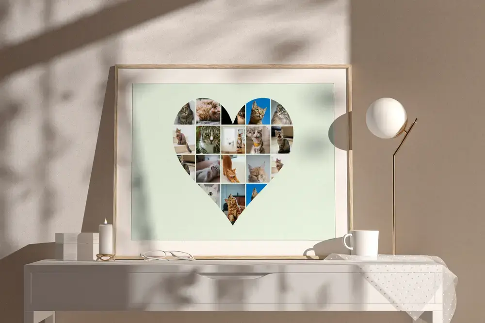 Heart-shaped cat photo collage on pale green in a natural wood frame, resting on a white sideboard beside a lamp