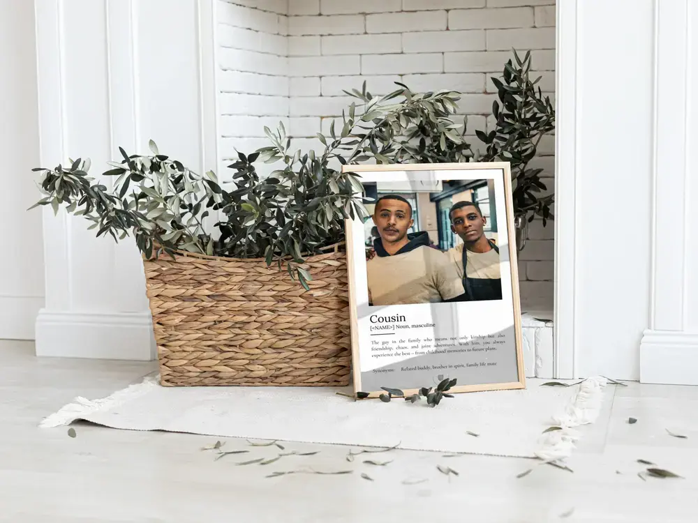 Framed cousin definition poster with one large photo, resting on the floor beside a woven basket of greenery
