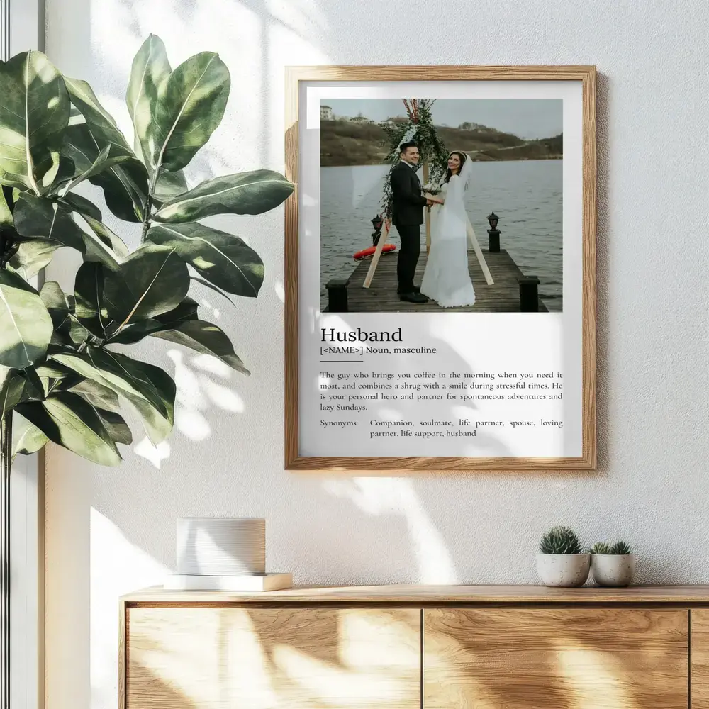Wood-framed husband definition poster with a wedding portrait, hanging above a cabinet beside a leafy plant