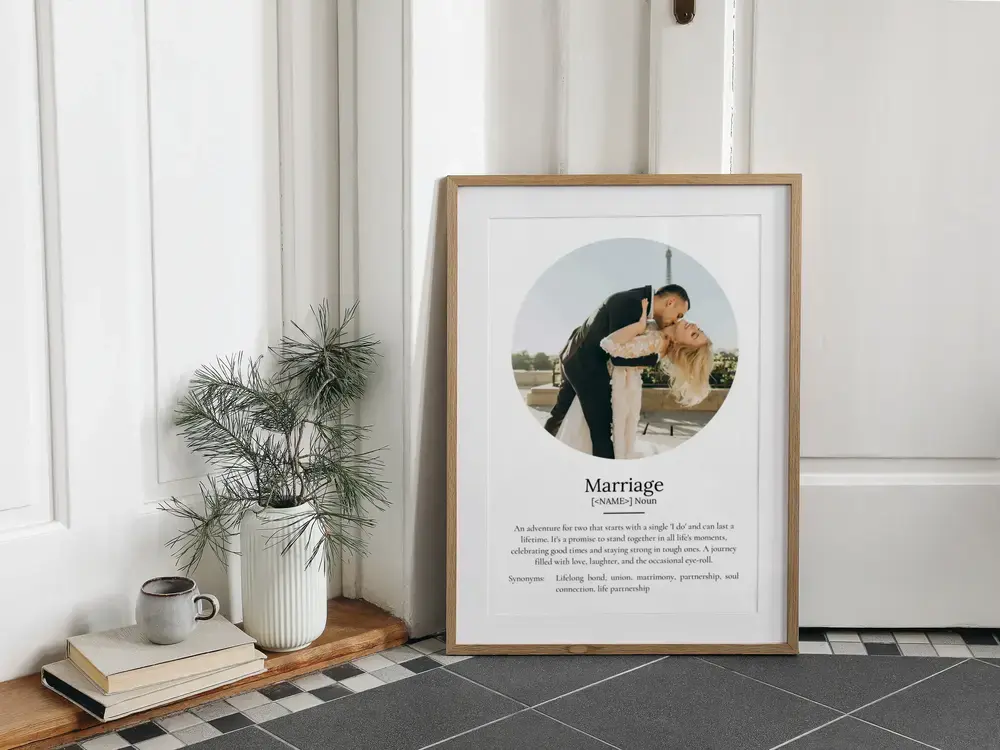 Marriage definition poster with a circular wedding photo in a wood frame, resting on a tiled floor beside a plant