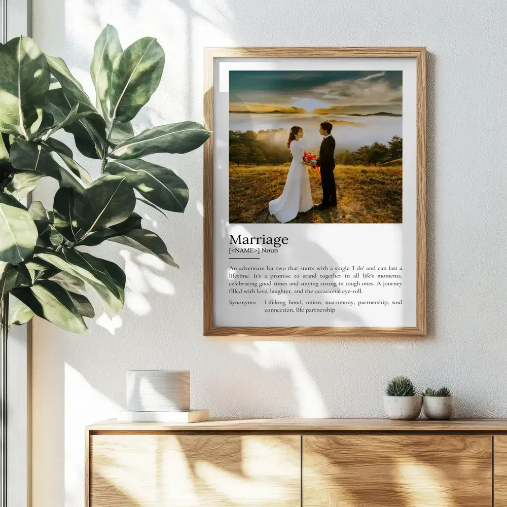 Wood-framed marriage definition poster with a wedding portrait, hung above a sideboard beside a leafy plant