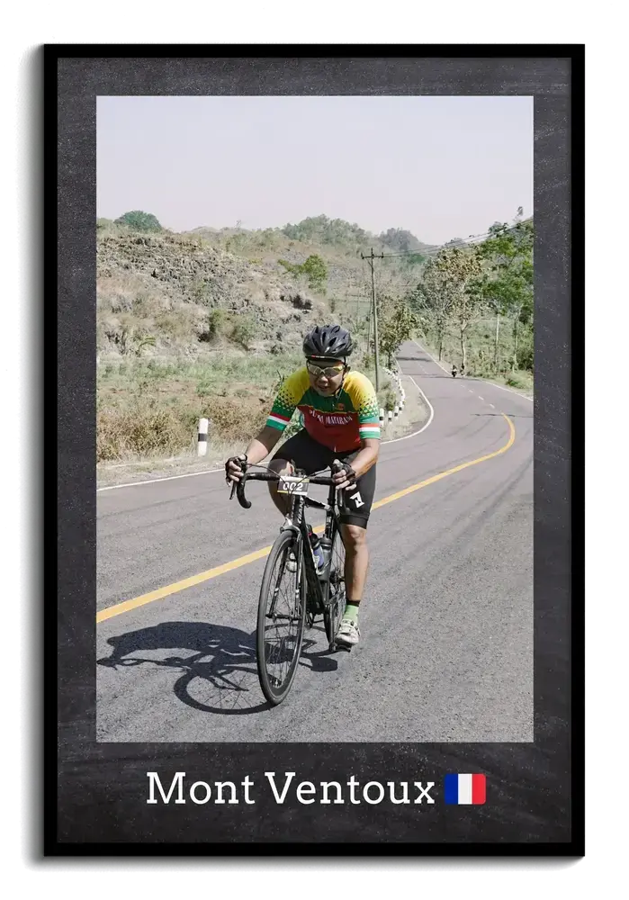 Road cycling photo on a mountain road with a location caption and flag, displayed in a black frame
