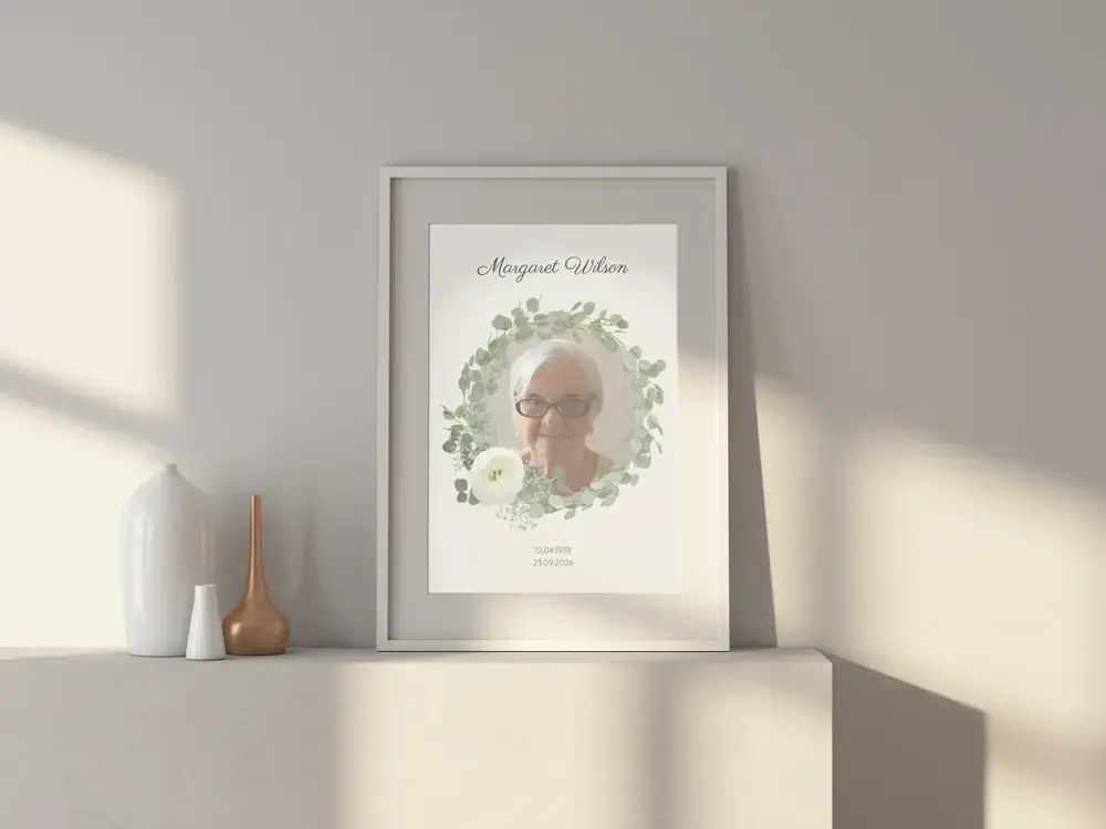Memorial portrait with a leafy wreath and personalized name, in a white frame on a sunlit sideboard