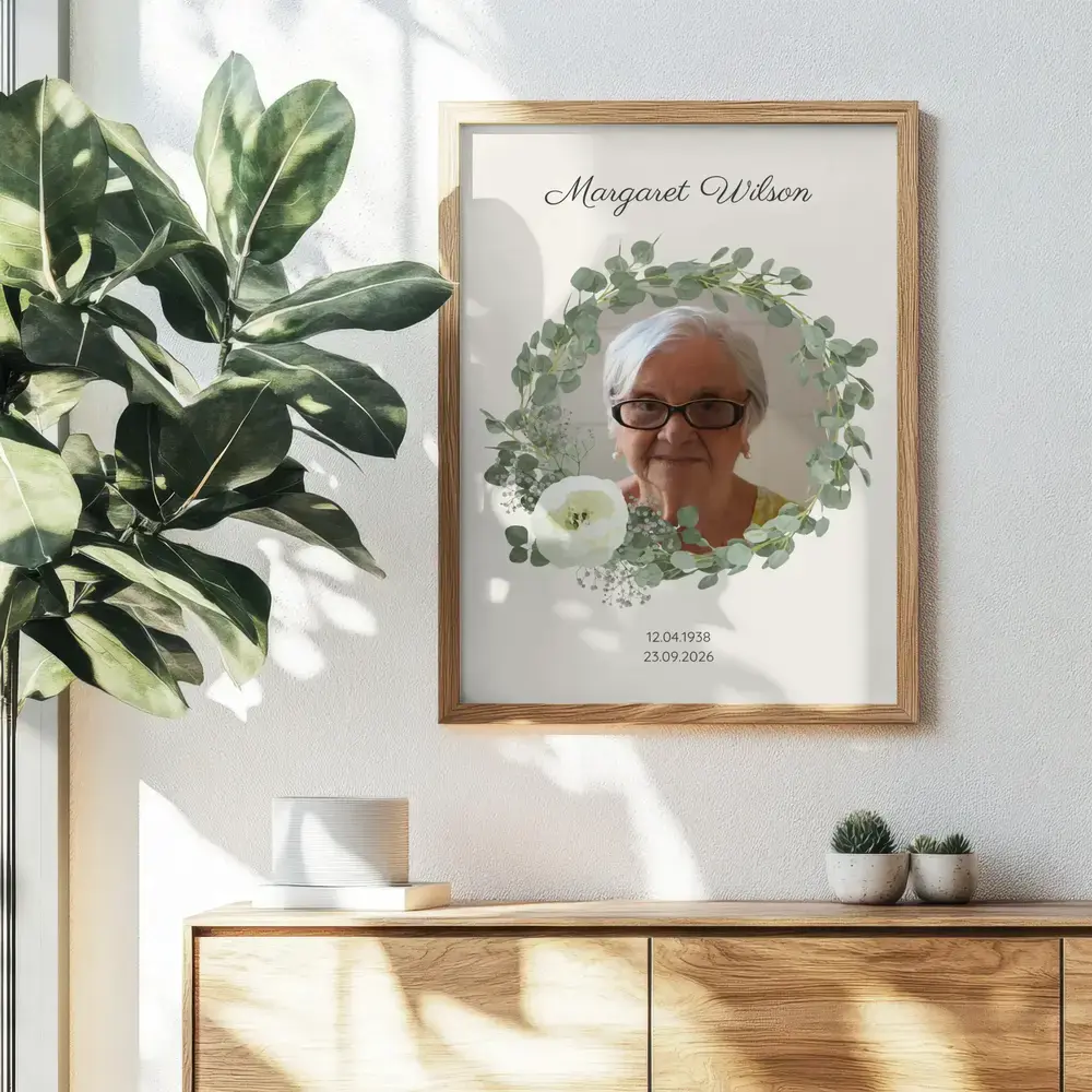 Memorial portrait with an eucalyptus wreath and white flowers, framed in natural wood above a sideboard