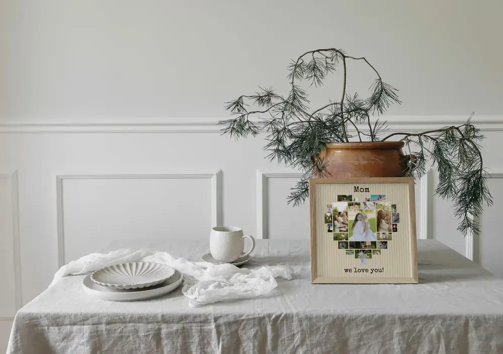 Heart-shaped photo collage in a light wood frame on a table beside a vase, a Mother's Day gift