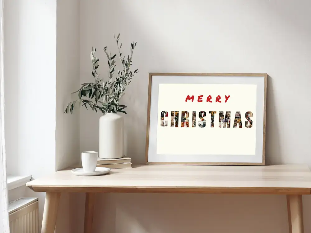 Framed Christmas photo collage with family photos forming letters, displayed on a wooden desk beside a vase
